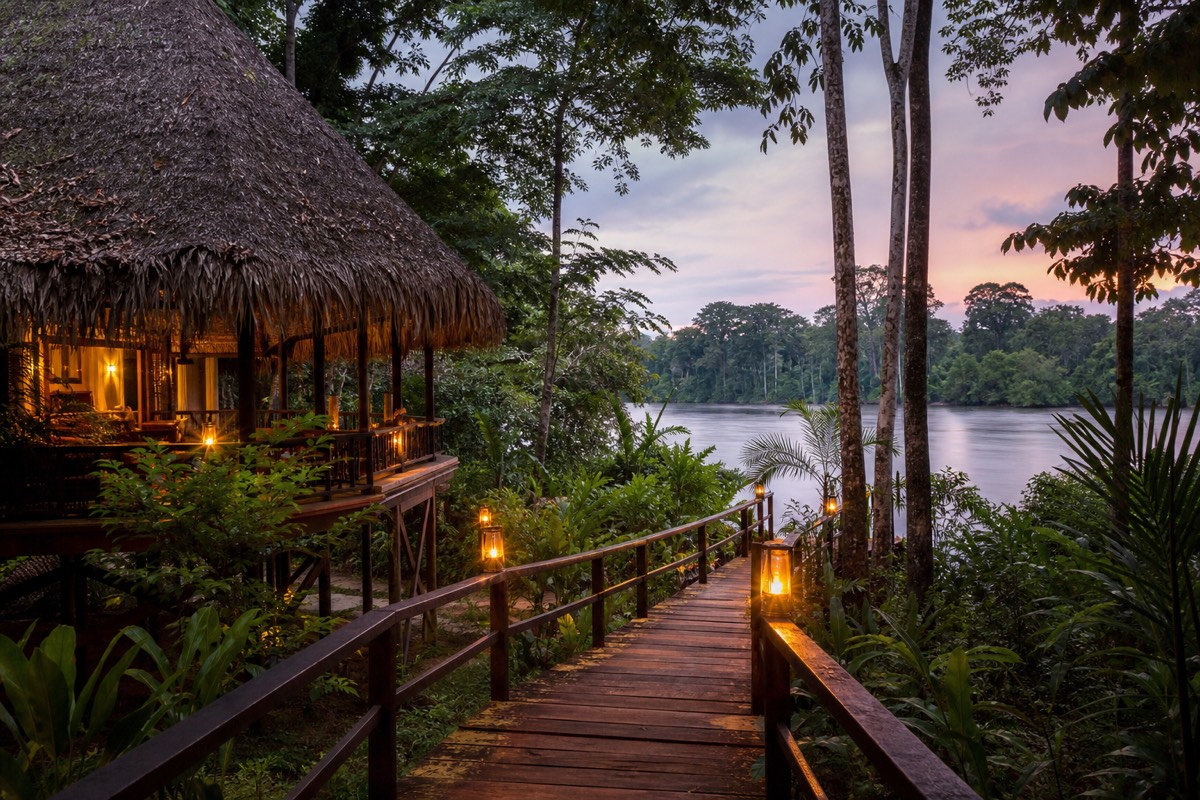 A stilted Amazon lodges near Iquitos scene, with a jungle lodge glowing at dusk above the river in Peru